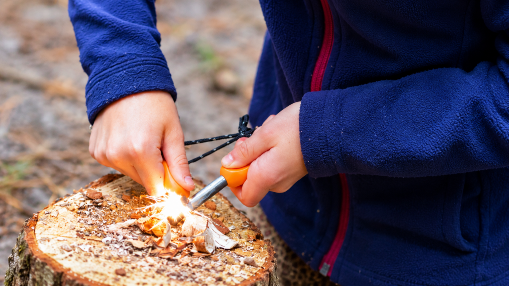 Handen maken vuur met een firesteel en houtkrullen tijdens het bushcraften bij Bos Ruimte in Zundert.